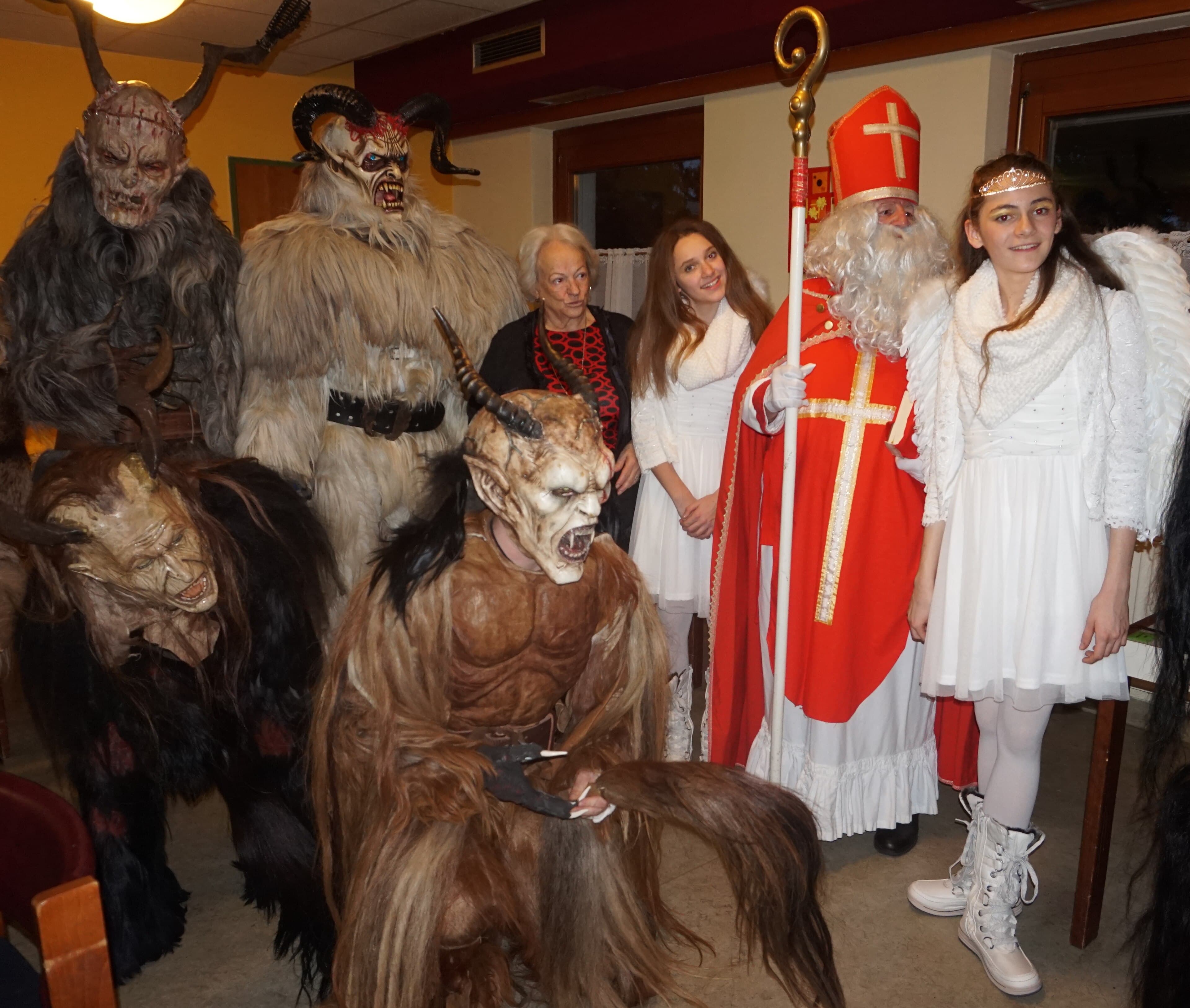 Performers in elaborate horned Krampus costumes with bells and furry suits marching through a town square