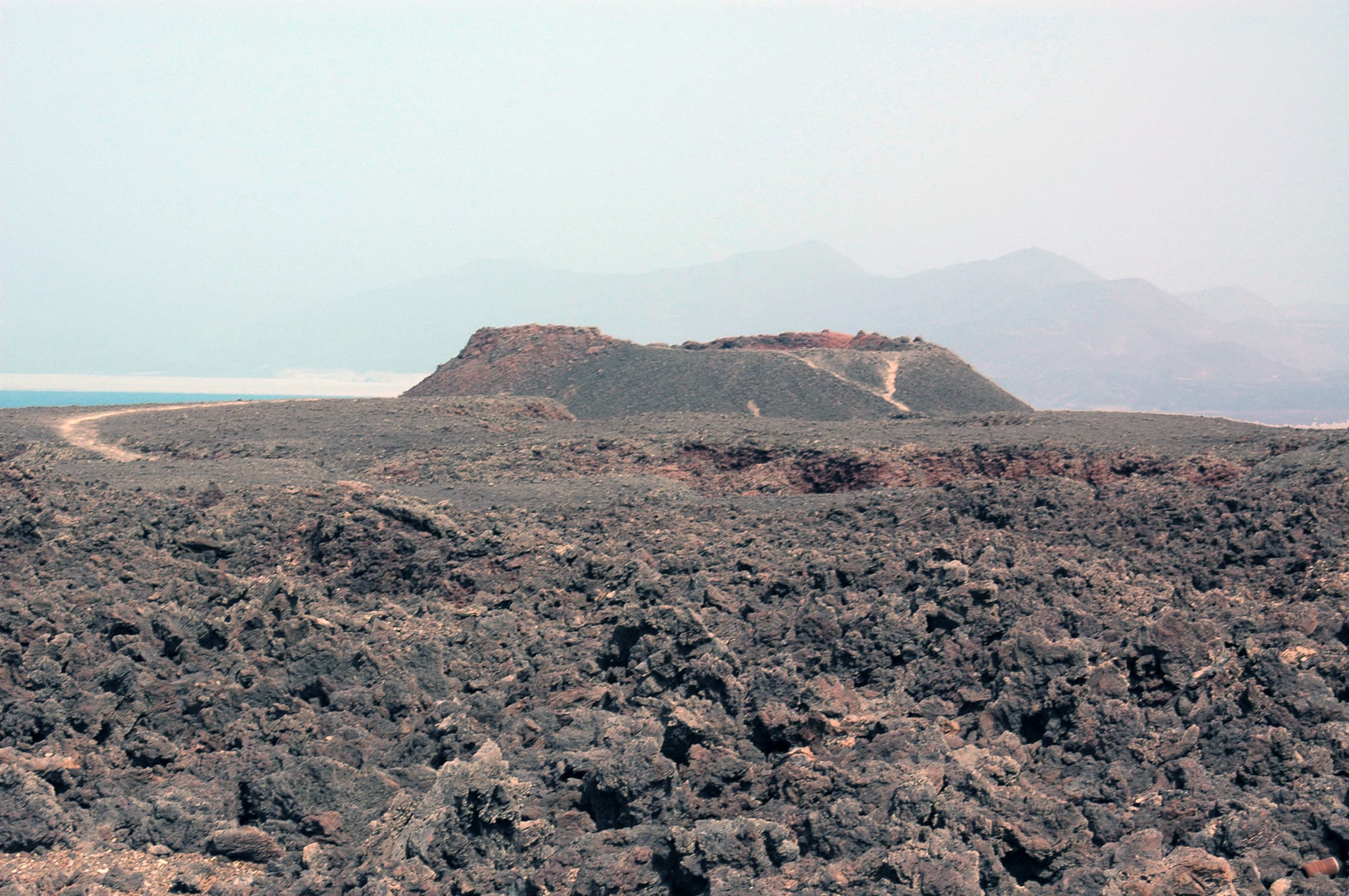 The dark lava fields and cone of Ardoukoba volcano under a wide sky in Djibouti