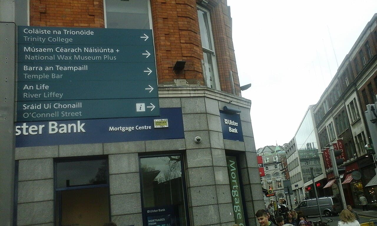 A green road sign in Ireland showing place names in Irish and English