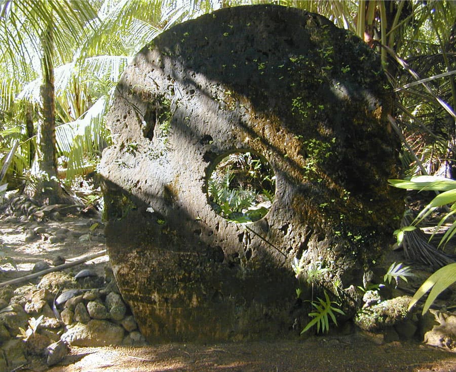A row of large circular stone discs standing upright against a wall on Yap island