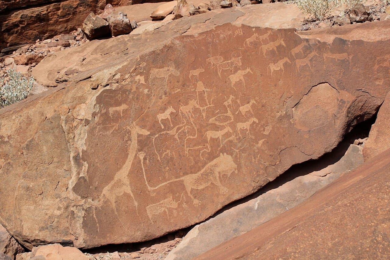Ancient rock engravings of animals carved into a flat stone surface in a desert landscape