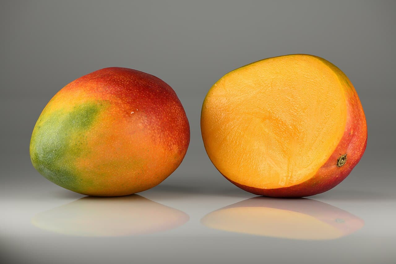 Two mangoes - one whole and one cut in half showing the bright orange flesh